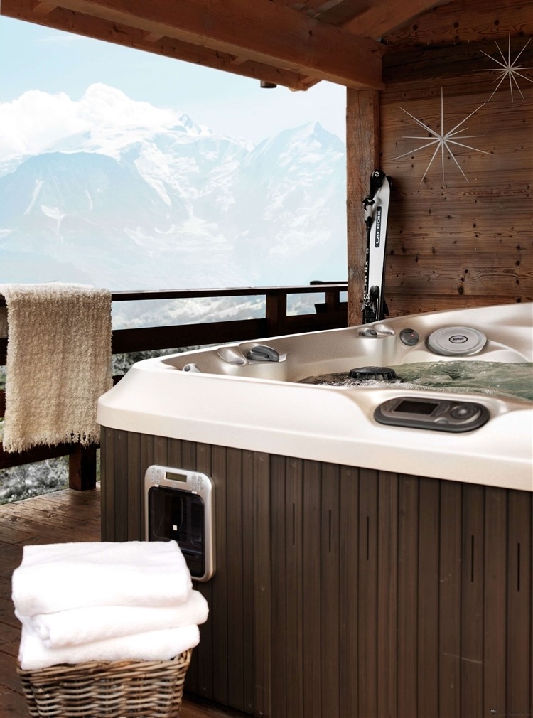 Jacuzzi installé sur la terrasse couverte de ce chalet en bois alpin jacuzzi chalet montagnard alpes ski