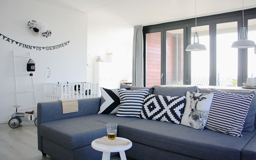 Un confortable et moderne canapé d’angle en gris sur un fond blanc constitue le point central du décor de la pièce salon séjour appartement jeune couple design scandinave