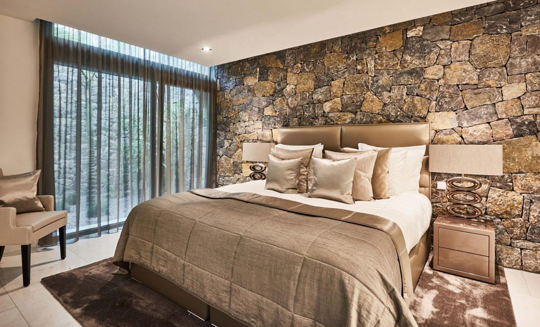 La suite des maitres est décorée avec des pierres locales spécialement taillées pour apporter une touche rustique à l’ambiance chambre moderne et rustique mur en pierre villa de luxe