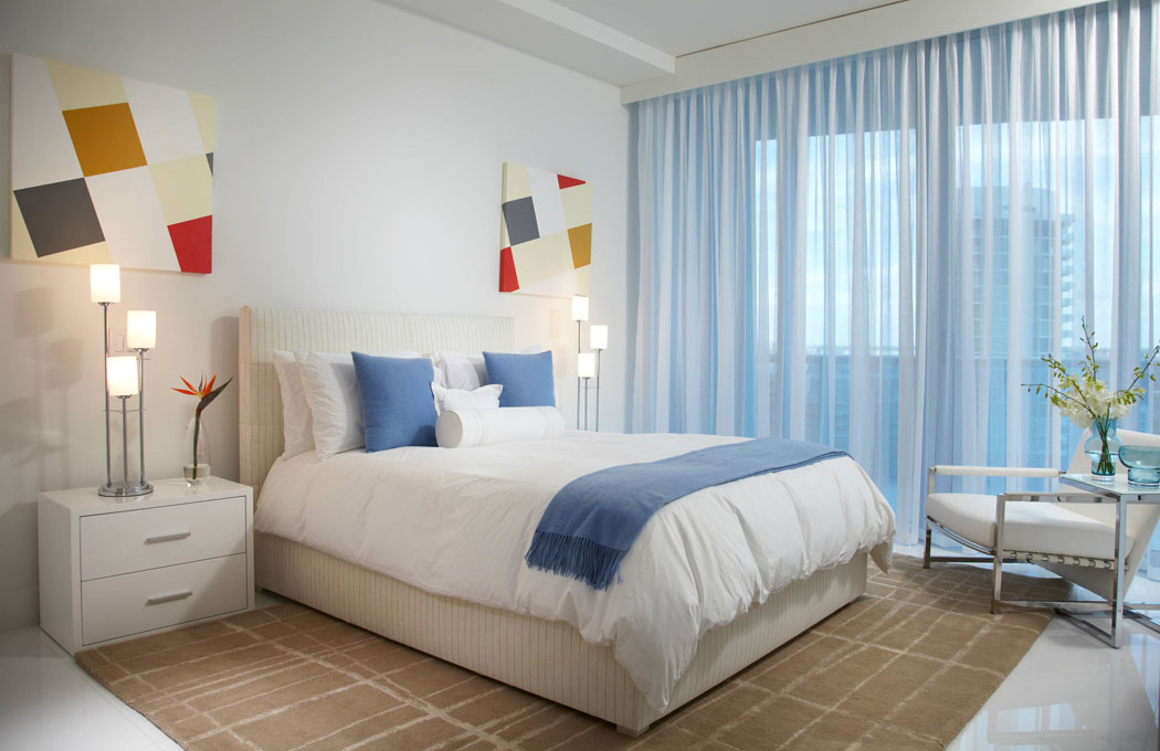 Une des chambres de cette résidence secondaire avec la baie vitrée menant vers le balcon et la vue exotique sur la plage grande et élégante chambre design déco blanc et bleu
