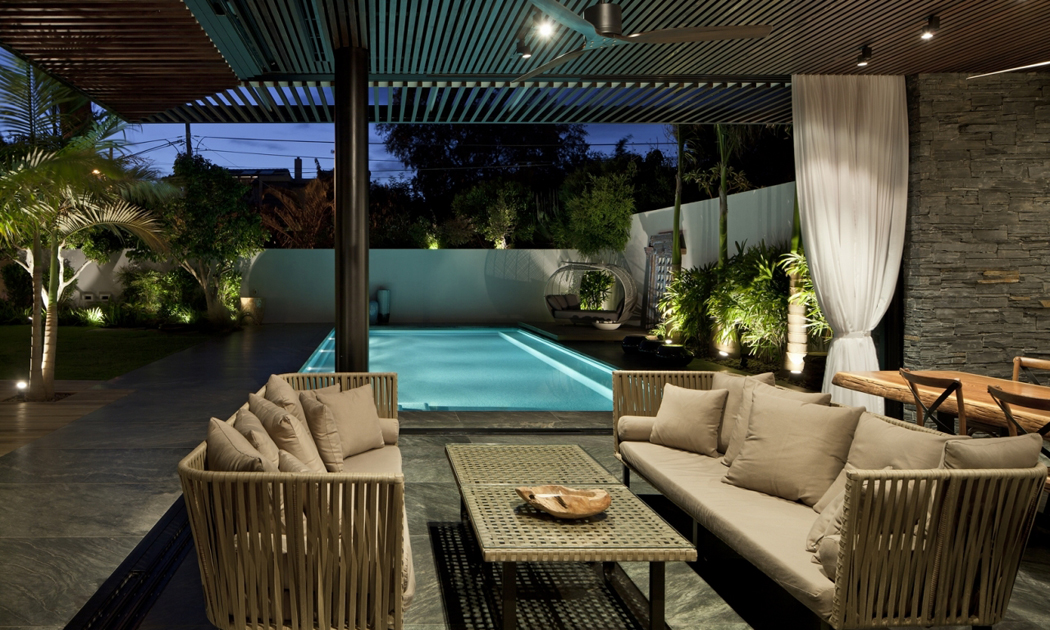Terrasse couverte par une pergola avec un coin « séjour » et un coin « salle à manger » terrasse et la piscine éclairées maison de ville
