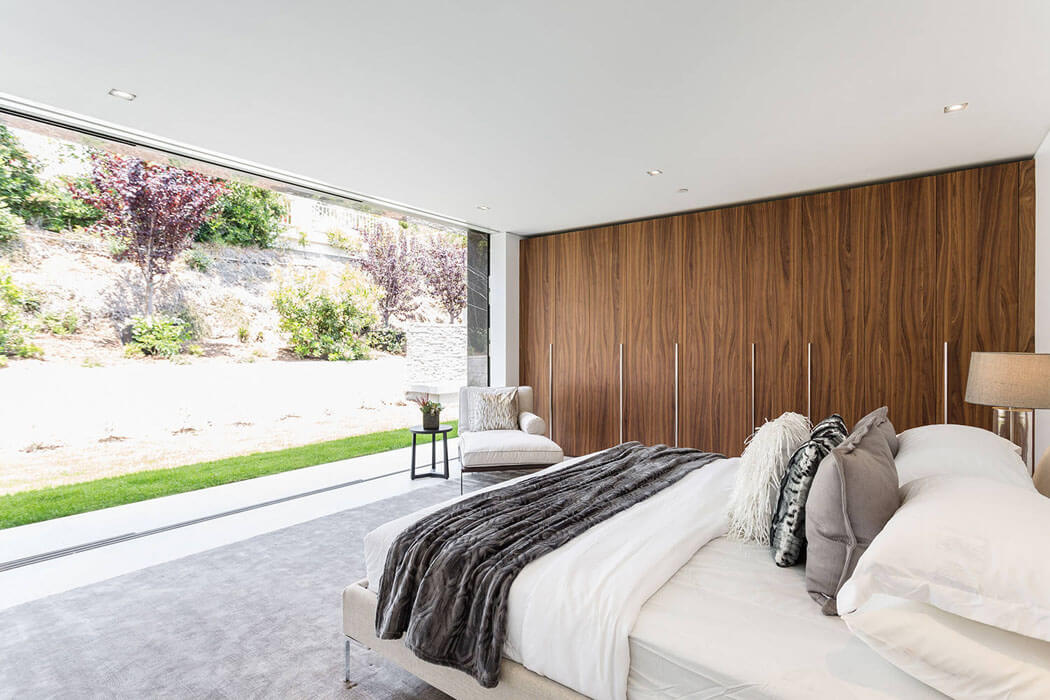 Située dans l’arrière de cette résidence de haut standing, une autre chambre donne sur le jardin et la haie de la propriété grandes ouvertures baies chambre moderne luxe